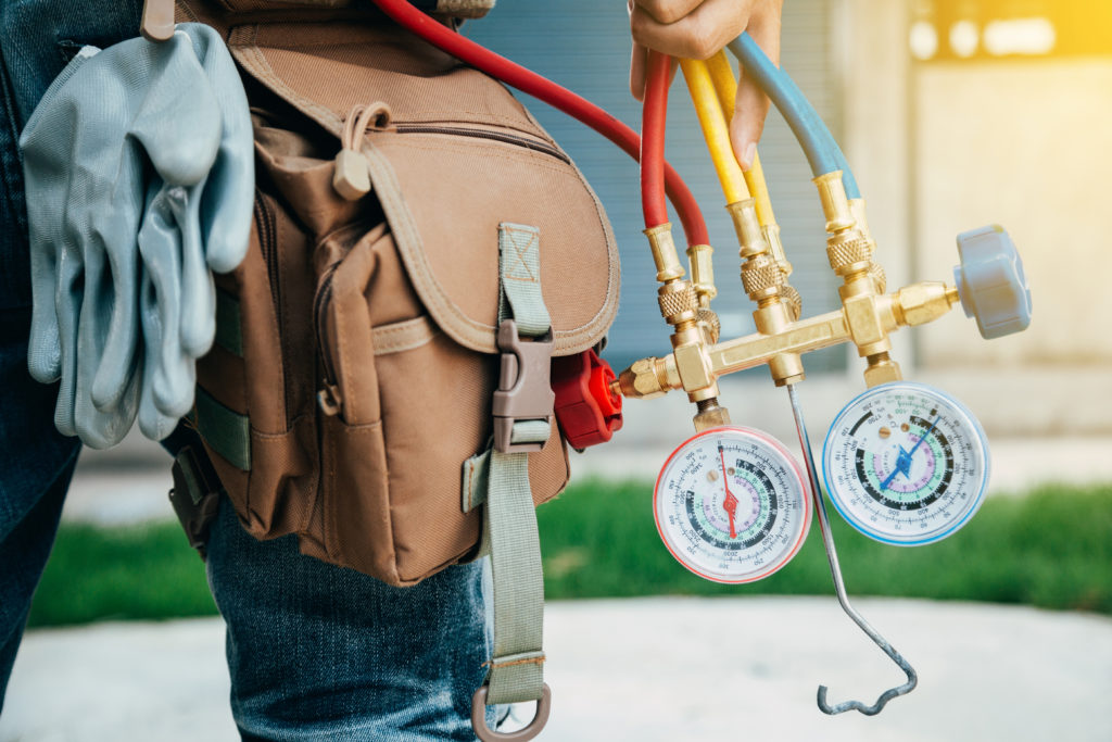 Close up of a technician's hip with a toolbelt and hand holding gauges