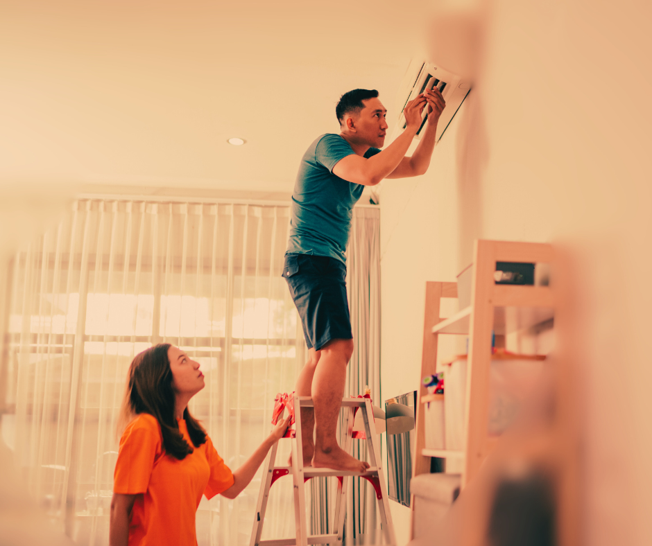 Man attempts to repair a mini split air conditioner as his wife watches