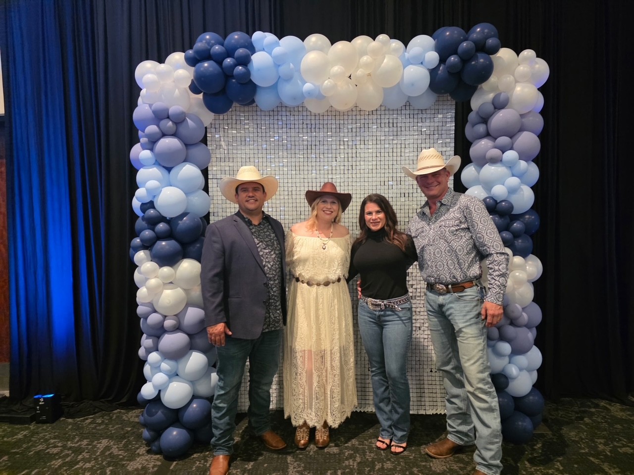 Four friends stand in front of a photo backdrop wearing Western clothes